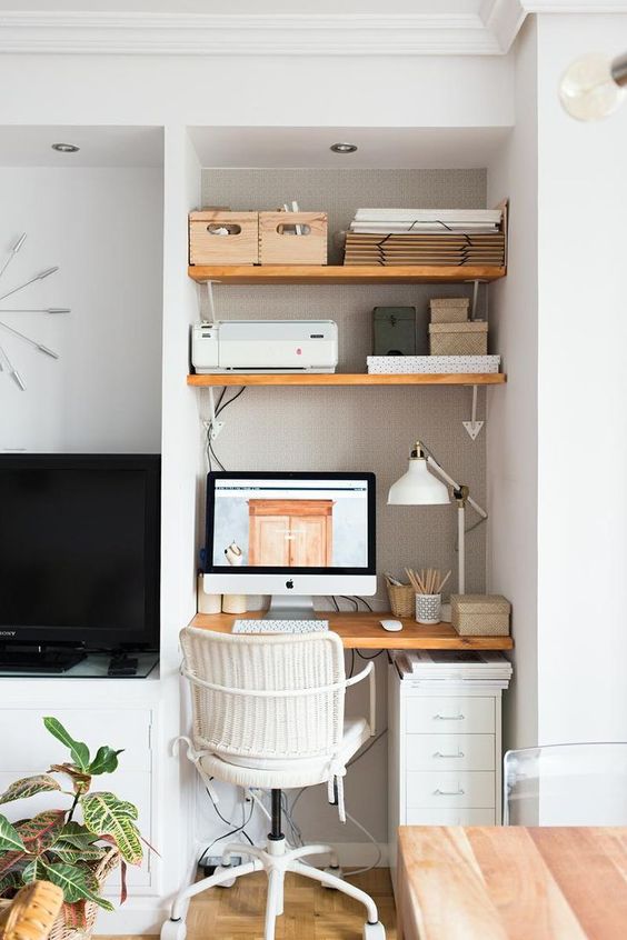 a small and chic home office nook in the living room, with wall-mounted shelves and a desk, a file cabinet, a PC and a lamp