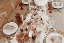 11 a gorgeous boho Thanksgiving tablescape with gold placemats and white porcelain, a lush table runner made of pampas grass, fronds, a white pumpkins, pink and white blooms