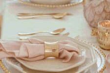 12 a blush and gold Thanksgiving tablescape with pink pumpkins, gold candleholders, gold rimmed plates and gold napkins rings and cutlery
