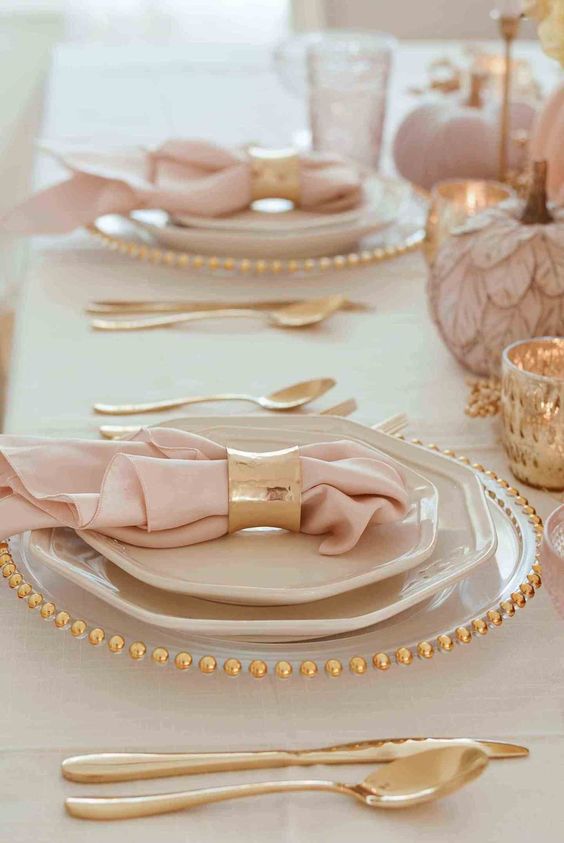 a blush and gold Thanksgiving tablescape with pink pumpkins, gold candleholders, gold rimmed plates and gold napkins rings and cutlery