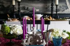 12 a bold and refined Thanksgiving tablescape with a purple table runner and candles, a blue napkin and glass, white blooms and greenery