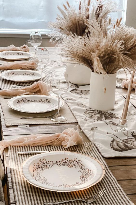 a neutral boho Thanksgiving tablescape with wheat and grass centerpieces, striped placemats, blush napkins and printed plates