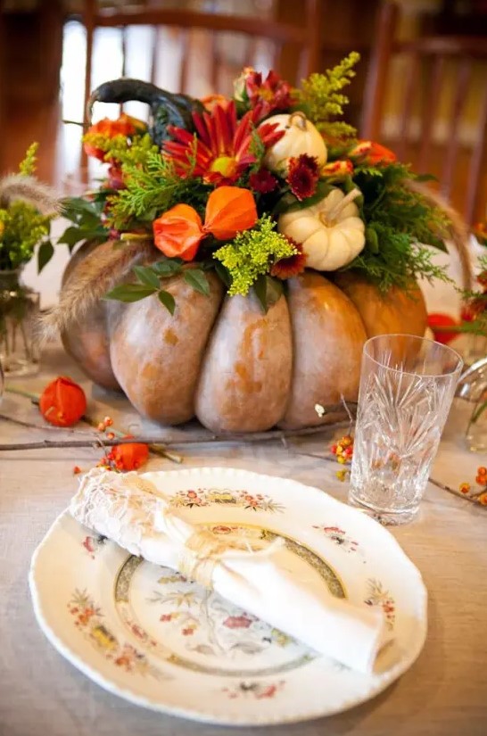 an oversized heirloom pumpkin with greenery, bright blooms and mini white pumpkins as a bold Thanksgiving centerpiece