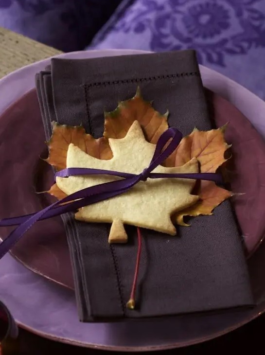 a bold purple place setting with bright purple fabric, purple layered plates, a brown napkin and a leaf cookie is amazing