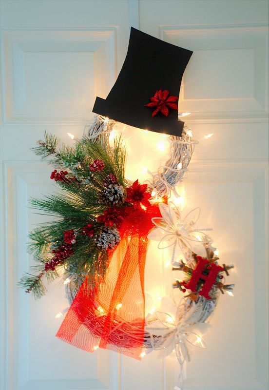 a lit up Christmas wreath shaped as a snowman with evergreens, berries and pinecones, a top hat and a monogram
