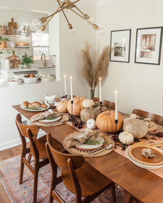 a neutral and very cozy Thanksgiving tablescape with a large runner and woven placemats, natural pumpkins and tall and thin candles