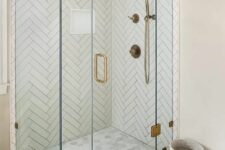 13 a shower space clad with herringbone and marble tiles, brass fixtures and a glass door with a brass handle