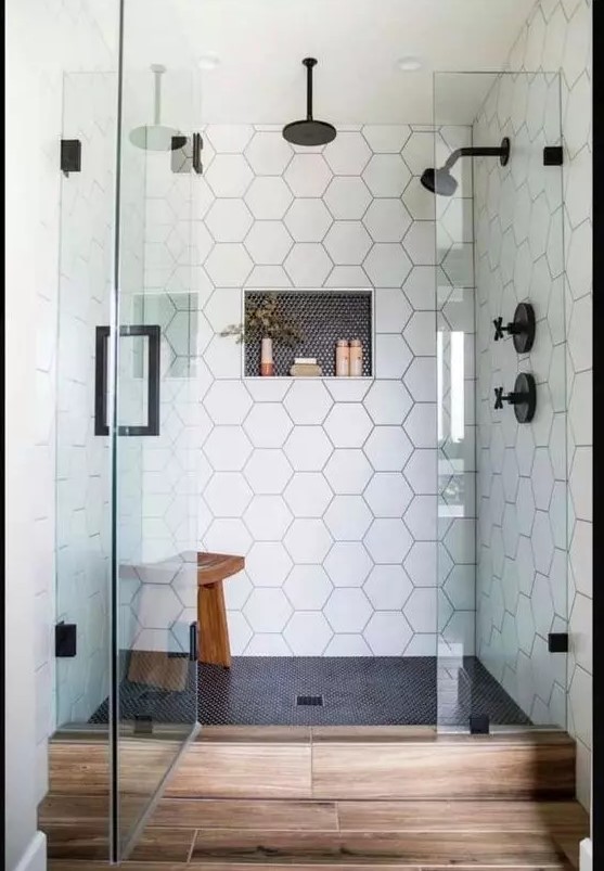 a chic shower space with black penny and white hex tiles, seamless glass doors with a black handle and black fixtures