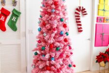 14 a hot pink Christmas tree decorated with super colorful ornaments and striped ribbons, topped with a gold star and with gifts