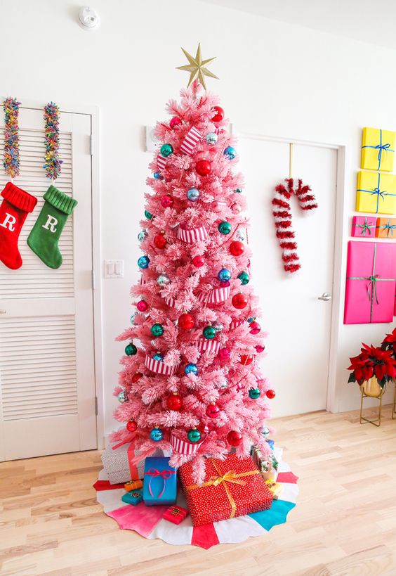 a hot pink Christmas tree decorated with super colorful ornaments and striped ribbons, topped with a gold star and with gifts