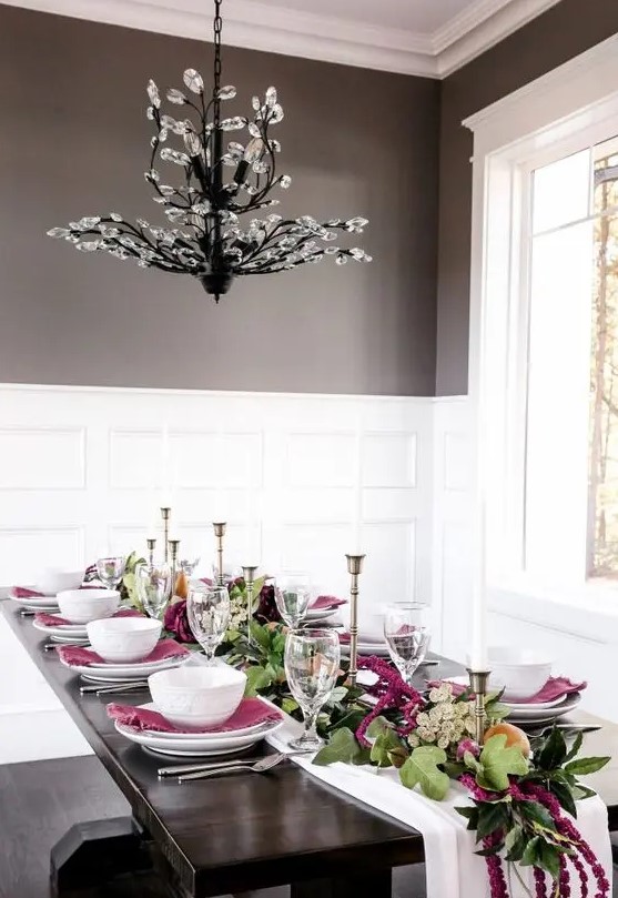 a bright modern Thanksgiving tablescape with a white runner, greenery and purple blooms, candles, purple napkins and white porcelain