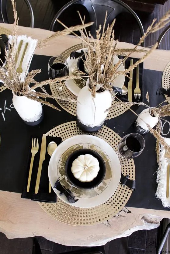 a chic black and gold Thanksgiving tablescape with a dark runner, napkins, plywood placemats, wheat in a vase and gold cutlery