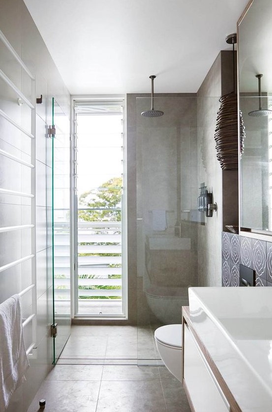 a contemporary bathroom clad with tan tiles, with a shower space enclosed in glass and a floor to ceiling window with frosted glass