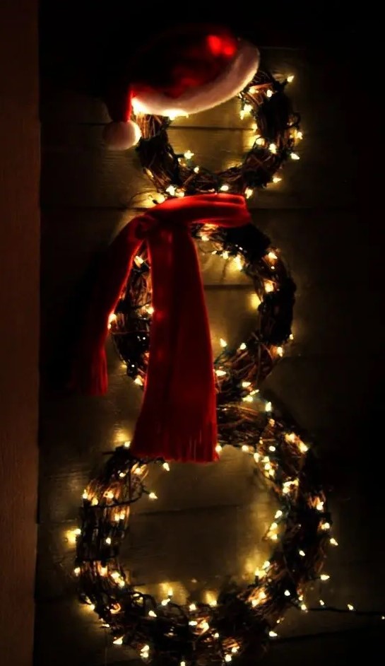 a snowman made of lit up wreaths and with a hat and a scarf is a creative alternative to a usual wreath for Christmas