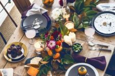 16 a bright Thanksgiving table setting with an uncovered table, a greenery and fruit runner, candles, blooms and black chargers
