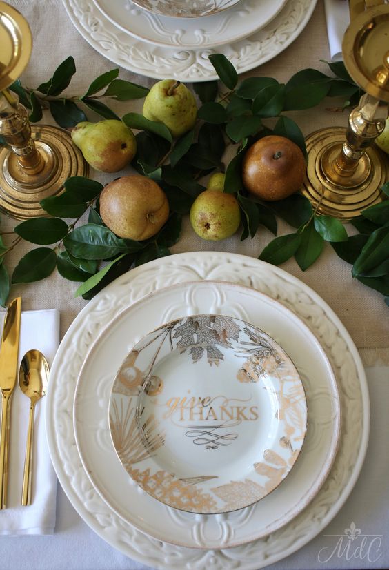 a chic rustic gold Thanksgiving tablescape with patterned plates, gold cutlery, pears and leaves on the table, gilded candleholders