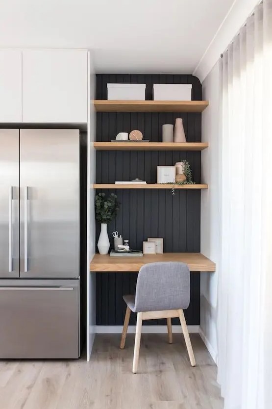 a small awkward nook with black shiplap, built in shelves and a desk, a comfy grye chair for working in the kitchen