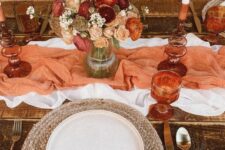 16 a warm-colored boho Thanksgiving tablescape with a white and orange table runner, a dried flower and pampas grass bouquet, a woven placemat and rust napkins