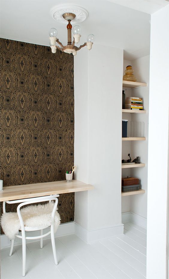 a small home office nook with a series of built in shelves, a desk and a white chair, an accent wall done with wallpaper