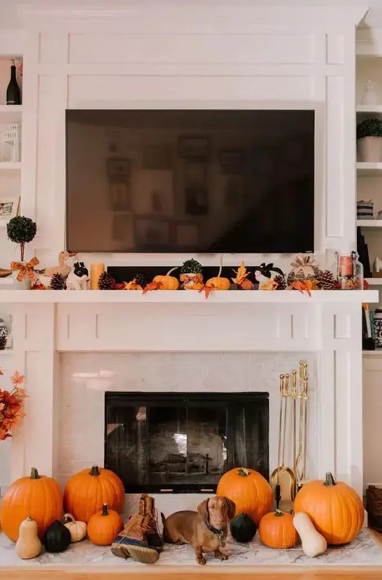 a lovely Thanksgiving mantel with bold leaves, candles, pinecones, small pumpkins on the mantel and larger ones next to the fireplace