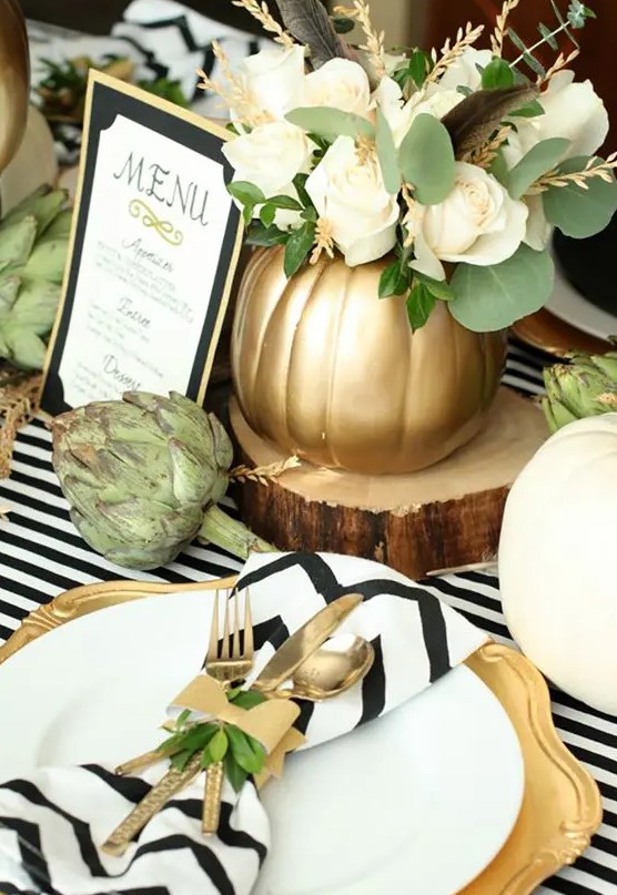 a modern rustic Thanksgiving tablescape with striped and chevron linens, gold chargers and cutlery, a white rose arrangement and artichokes