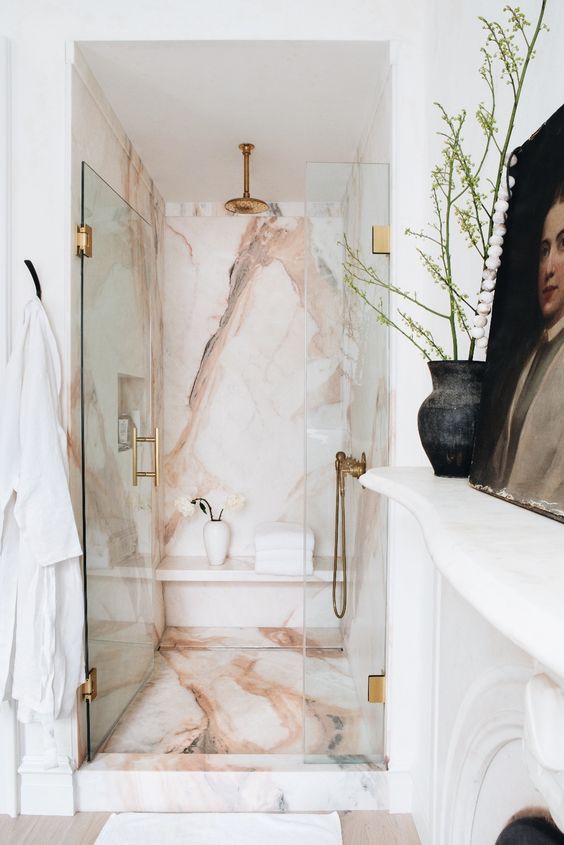 a refined neutral bathroom with a shower space clad with pink stone, with a glass door and brass fixtures is chic and glam