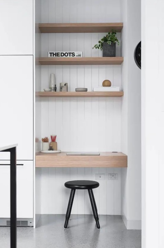 a small home office nook with built-in shelves, a built-in desk, a black stool and a potted plant and books