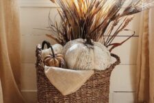 20 a boho Thanksgiving decoration of a basket with faux pumpkins, some grasses and wheat is a cool and cozy solution