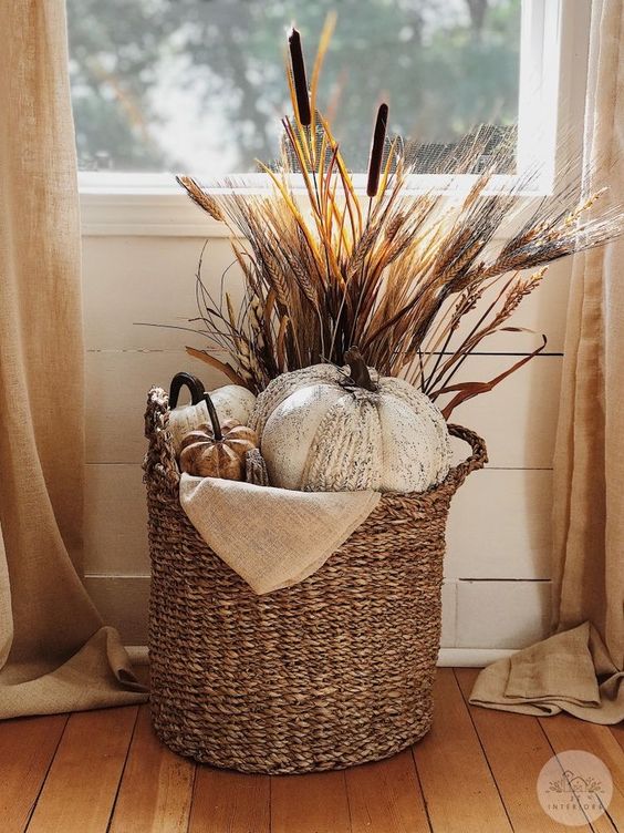 a boho Thanksgiving decoration of a basket with faux pumpkins, some grasses and wheat is a cool and cozy solution