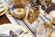 20 a cool black, white and gold Thanksgiving tablescape with a striped runner and napkin rings, gilded pumpkins, glasses and jars