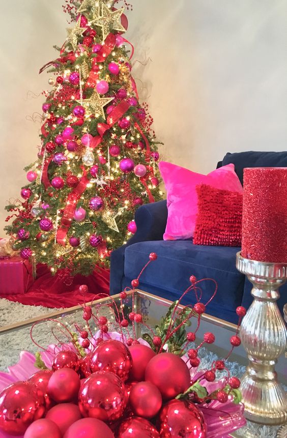 a shiny Christmas tree decorated with hot pink and red ornaments, lights, large gold stars and ribbons is wow