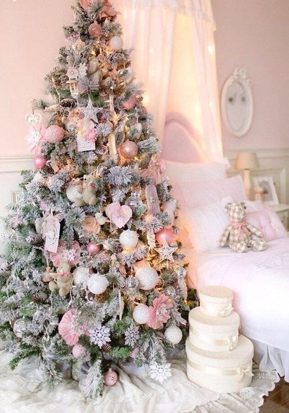 a flocked Christmas tree decorated with blush and pink ornaments, white snowflakes and stars and some paper decor
