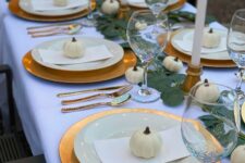 21 a modern Thanksgiving tablescape with gold chargers and candleholders plus cutlery, white porcelain and pumpkins, leaves and candles