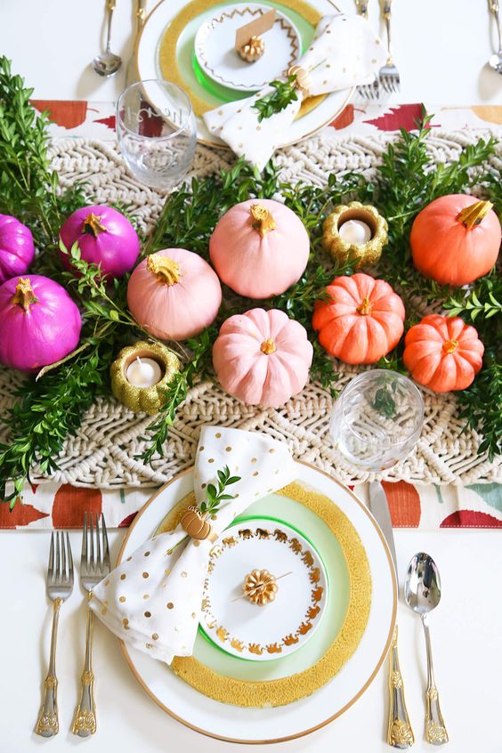 a colorful and glam Thanksgiving tablescape with a greenery and macrame runner, white gold rimmed plates, colorful pumpkins