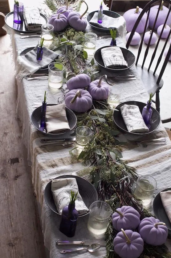 a creative and laid-back Thanksgiving tablescape with a linen striped tablecloth, a greenery runner, lilac pumpkins and lilac bottles with greenery