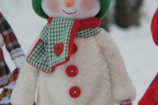 22 a dressed up snowman decoration in a white overall with buttons, a green hat and a green and red scarf is the cutest