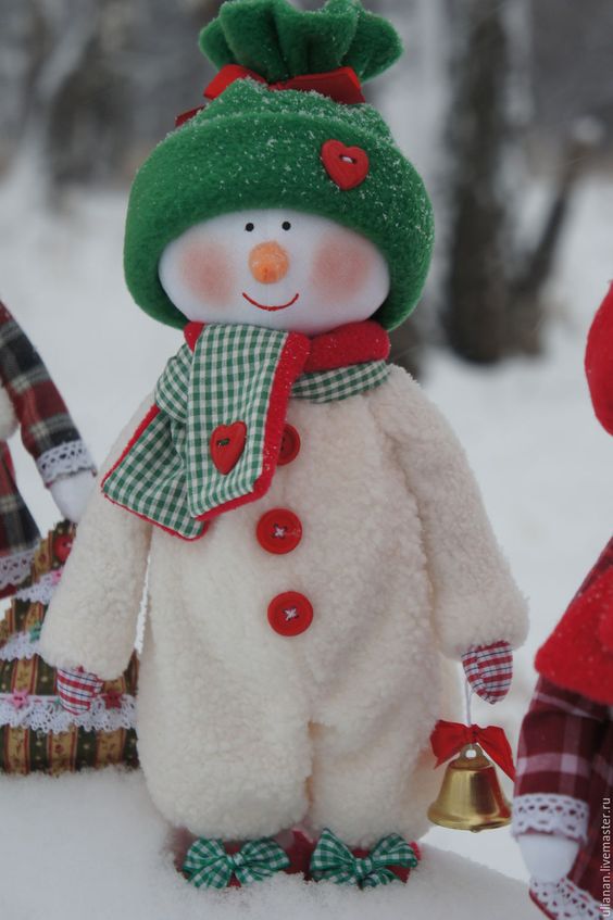 a dressed up snowman decoration in a white overall with buttons, a green hat and a green and red scarf is the cutest