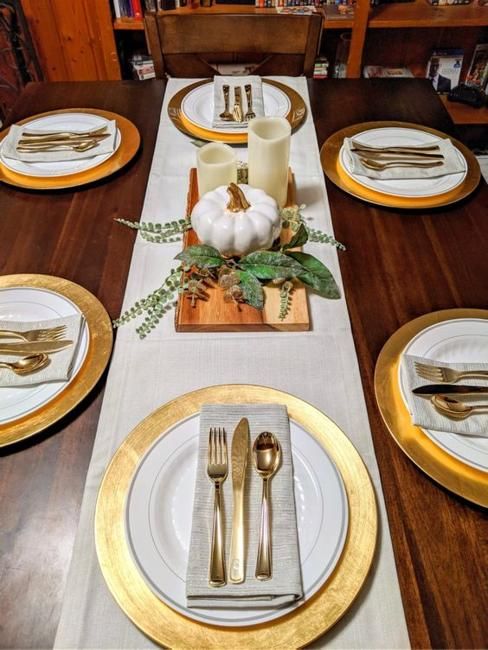 a pretty and simple Thanksgiving tablescape with gold chargers, a wooden plaque with candles and a pumpkin and gold cutlery