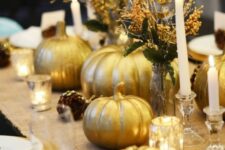 23 a pretty gold Thanksgiving tablescape with a burlap runner, gold pumpkins, gold candleholders, pinecones and candles, gilded leaves