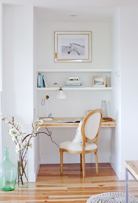 a small nook with built-in shelves and a desk, a white chair, an artwork and a pretty lamp is comfy for working