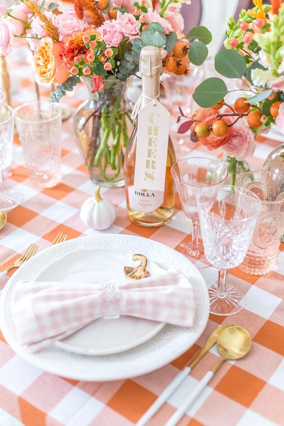 a cool blush and orange Thanksgiving tablscape with orange and pink blooms, white pumpkins and gold cutlery