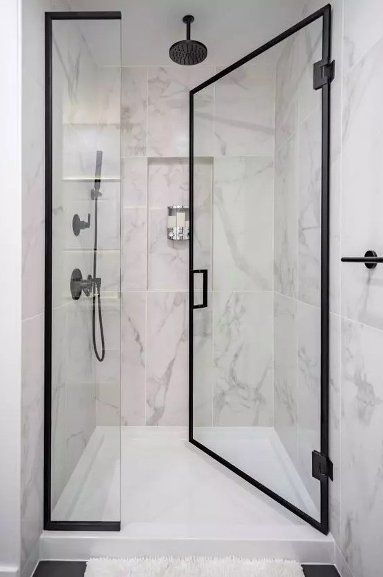 a chic shower space wiht large scale marble tiles, black frame glass doors and black fixtures is a lovely and cool space