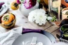 25 a laid-back and rustic Thanksgiving tablescape with greenery, bold purple blooms, fruits, black plates and purple napkins