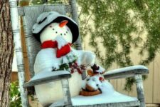 25 a rocker chair with a felt snowman in a bucket hat and a red scarf, branches and evergreens is a pretty vintage outdoor decor for Christmas