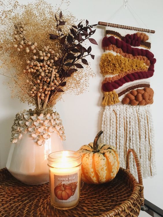 a bright fall woven hanging, a pumpkin and a candle, a vase with dried branches and berries for boho Thanksgiving decor