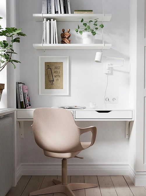 a small yet cool home office nook in the living room created with IKEA items   shelves, a desk and a blush chair plus a white sconce