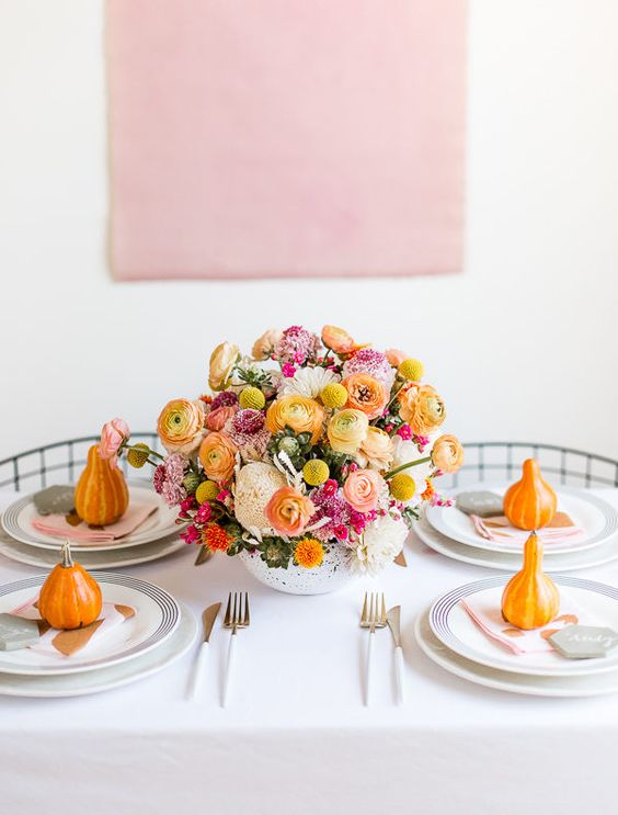 a modern and bright Thanksgiving tablescape with bold blooms in the center and orange pumpkins is amazing