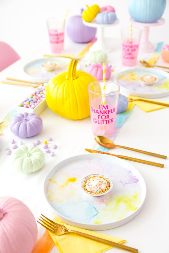 a pastel Thanksgiving tablescape with watercolor plates, pastel pumpkins and a runner, pastel candies and gold cutlery