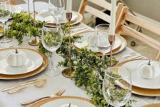 28 a stylish Thanksgiving table setting with gold chargers and cutlery, candleholders, mini white pumpkins and greenery
