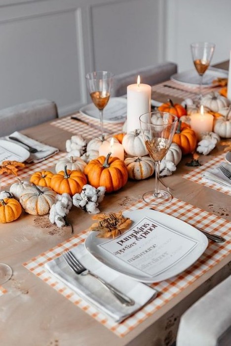 a cozy and bright Thanksgiving centerpiece of white and orange pumpkins, pillar candles and cotton